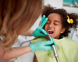 Dental hygienist cleaning child's teeth with special tools