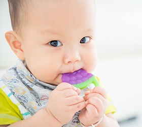An infant using a teether to bite down on that looks like grapes 