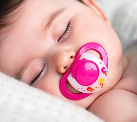 A baby lying asleep with a pink pacifier in its mouth