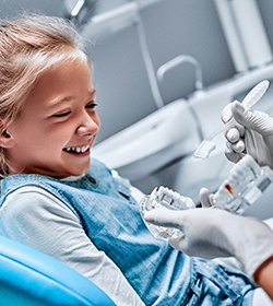 A young girl watching a dentist properly brush a mouth mold to show her the proper technique