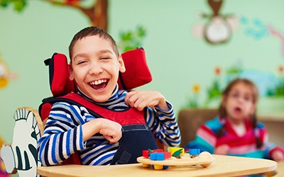A young boy wearing a striped shirt and seated in a wheelchair playing with toys
