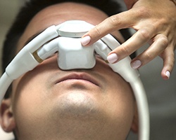 A male patient lying back in the dentist’s chair while a dentist points to the nasal mask to show how it works