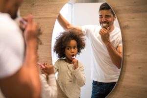 father and daughter brush teeth together in front of mirror