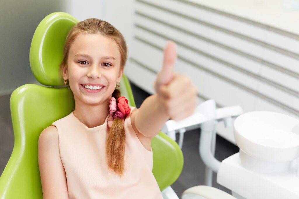 child smiling and giving thumbs up while visiting pediatric dentist 