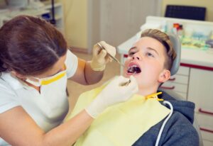 Teenager with brown hair and a grey hoodie in getting a checkup by a dentist wearing yellow gloves